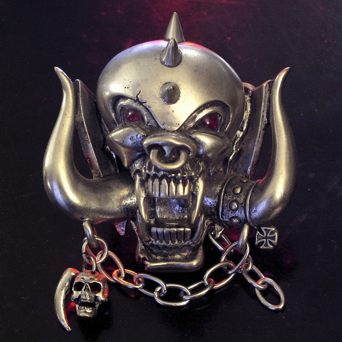 Silver belt buckle of the Motörhead Snaggletooth face with tusks, fangs, a spike on top and hanging chains